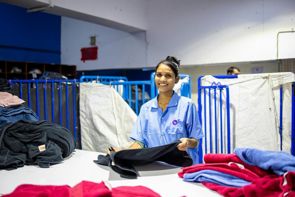 A smiling female textile worker folding clothes inside a factory setting, showcasing the blue-collar work environment.